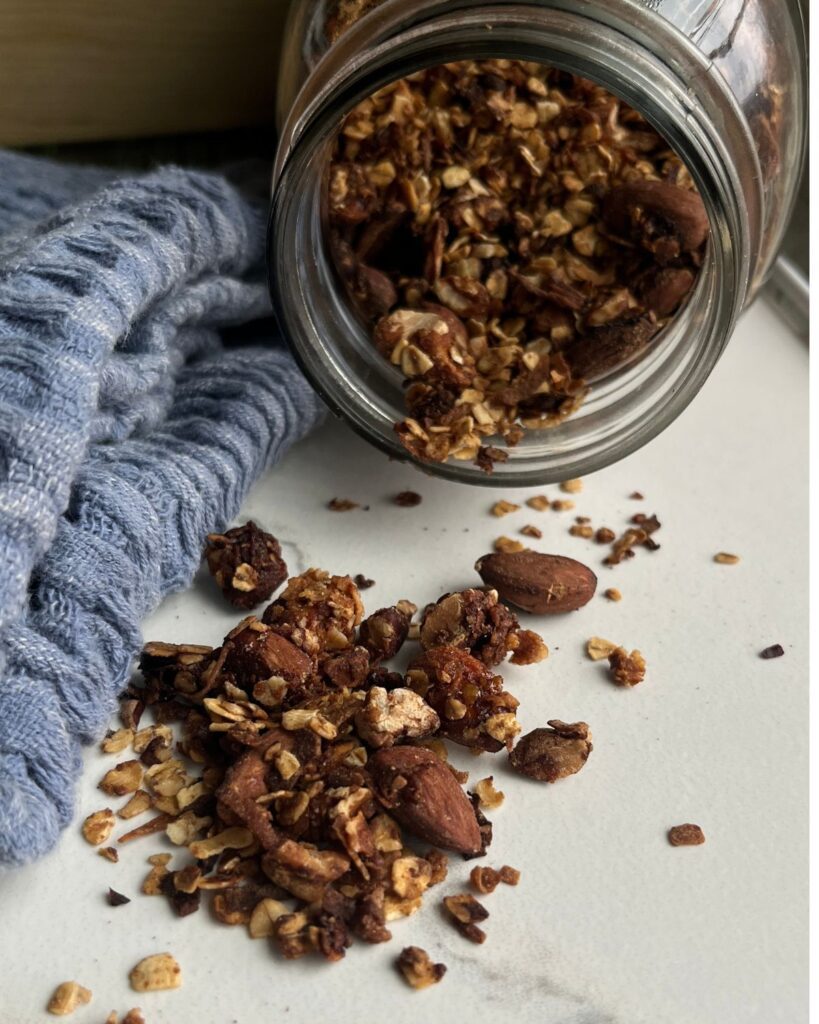 homemade granola spilling out of a glass jar onto a table