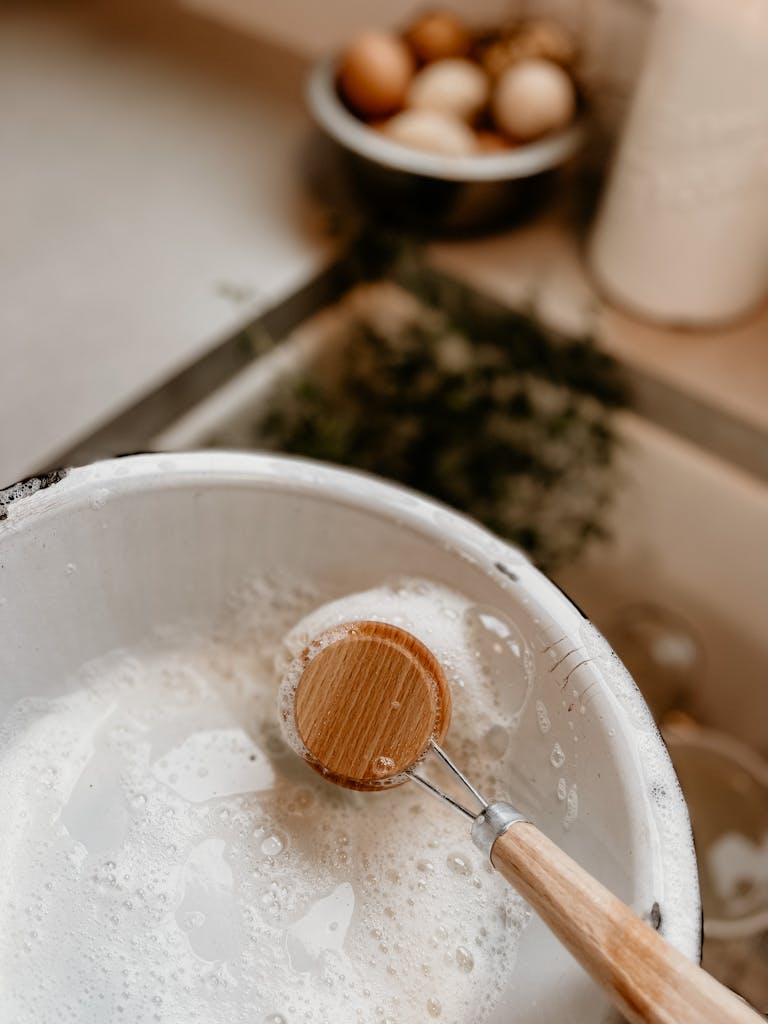 Close-up of a wooden spoon in a foamy bowl in an indoor kitchen setting.