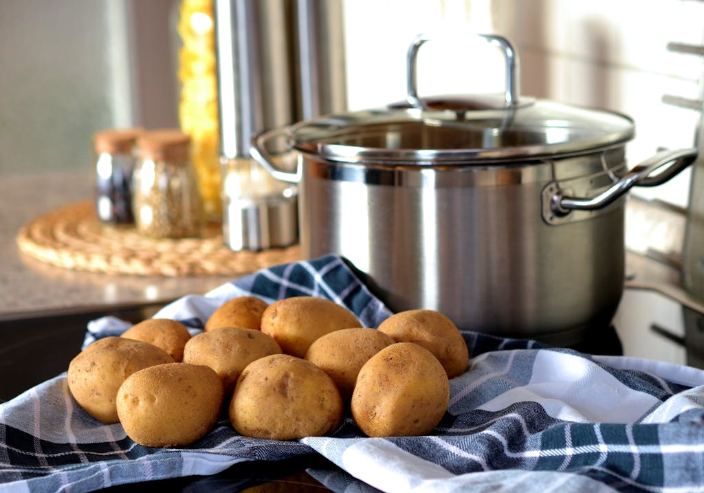 Fresh potatoes on cloth beside a stainless pot, ready for cooking in a modern kitchen.