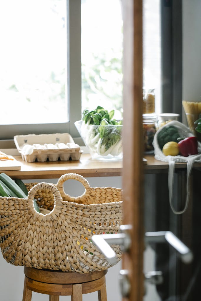 Wicker basket placed on stool near counter with eggs and vegetables in light kitchen