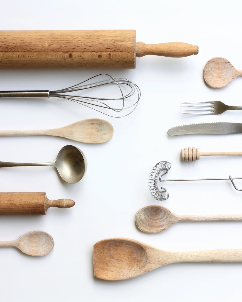 Wooden and metal kitchen utensils arranged on a white backdrop in a flat lay style.