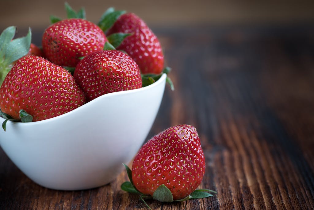Close-up of fresh strawberries in a white bowl on a rustic wooden table, highlighting vibrant red color.