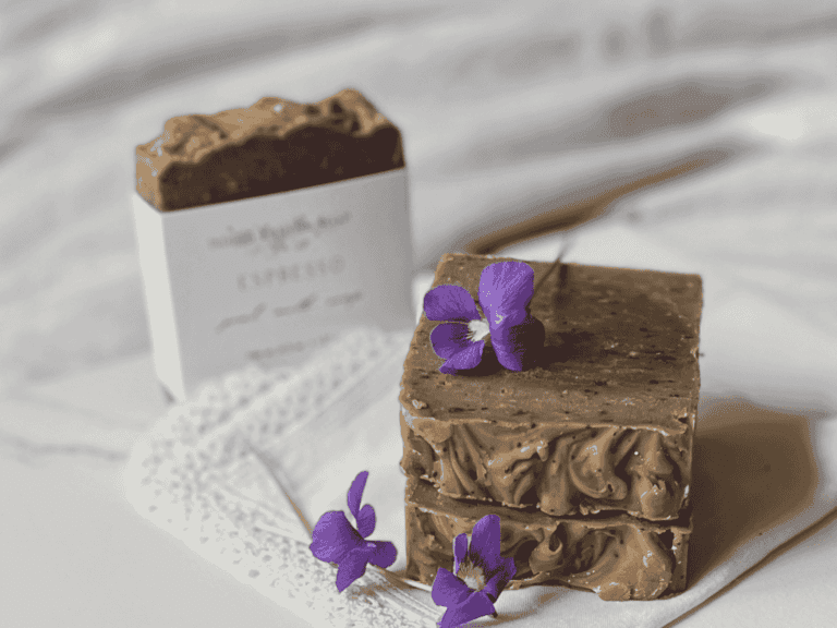 Coffee soap sitting on a white background with violets around them