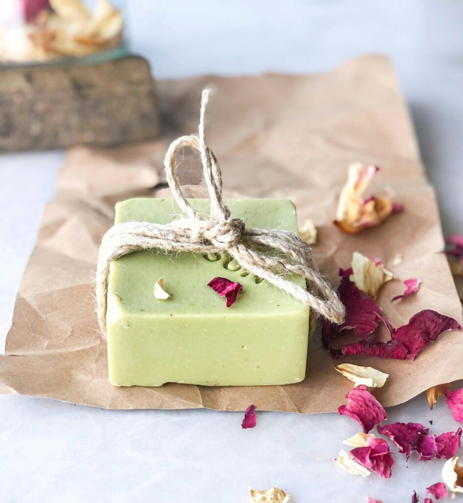 Handcrafted green soap bar wrapped with twine, surrounded by dried petals for a rustic feel.