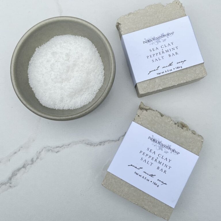 Two gray salt bars sitting on a white marble table with a gray bowl of white sea salt sitting next to them.