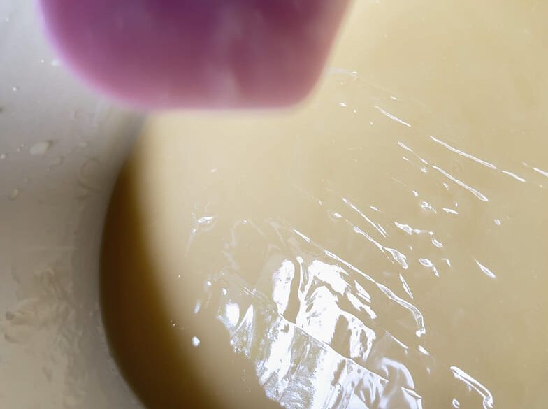 Soapmaker drizzling oil across soapbatter