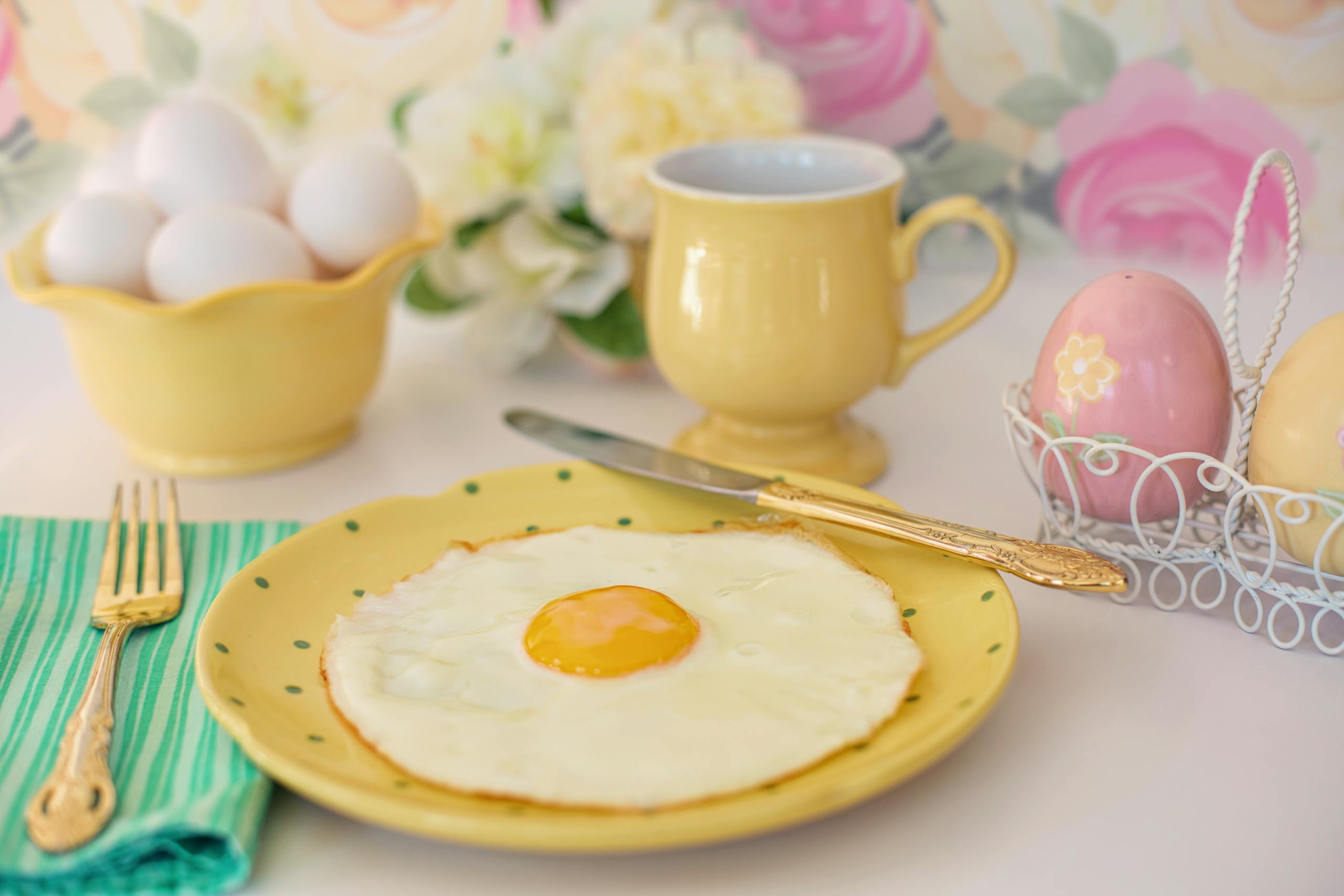 Bright breakfast setting with a fried egg, decorative vase, and pastel cups.